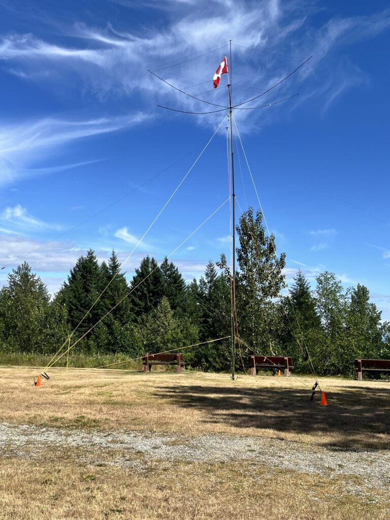 The BuddiHEX atop the fully extended mast, with the 40/80 metre dipole ends tied off to the park benches. Photo: Janice (VA7JMO)